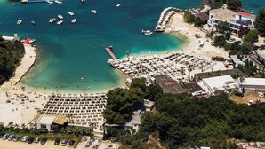 An aerial view of a coastal area with a beach, boats, and a marina. - Luxury Villa Oasis (Ksamil)
