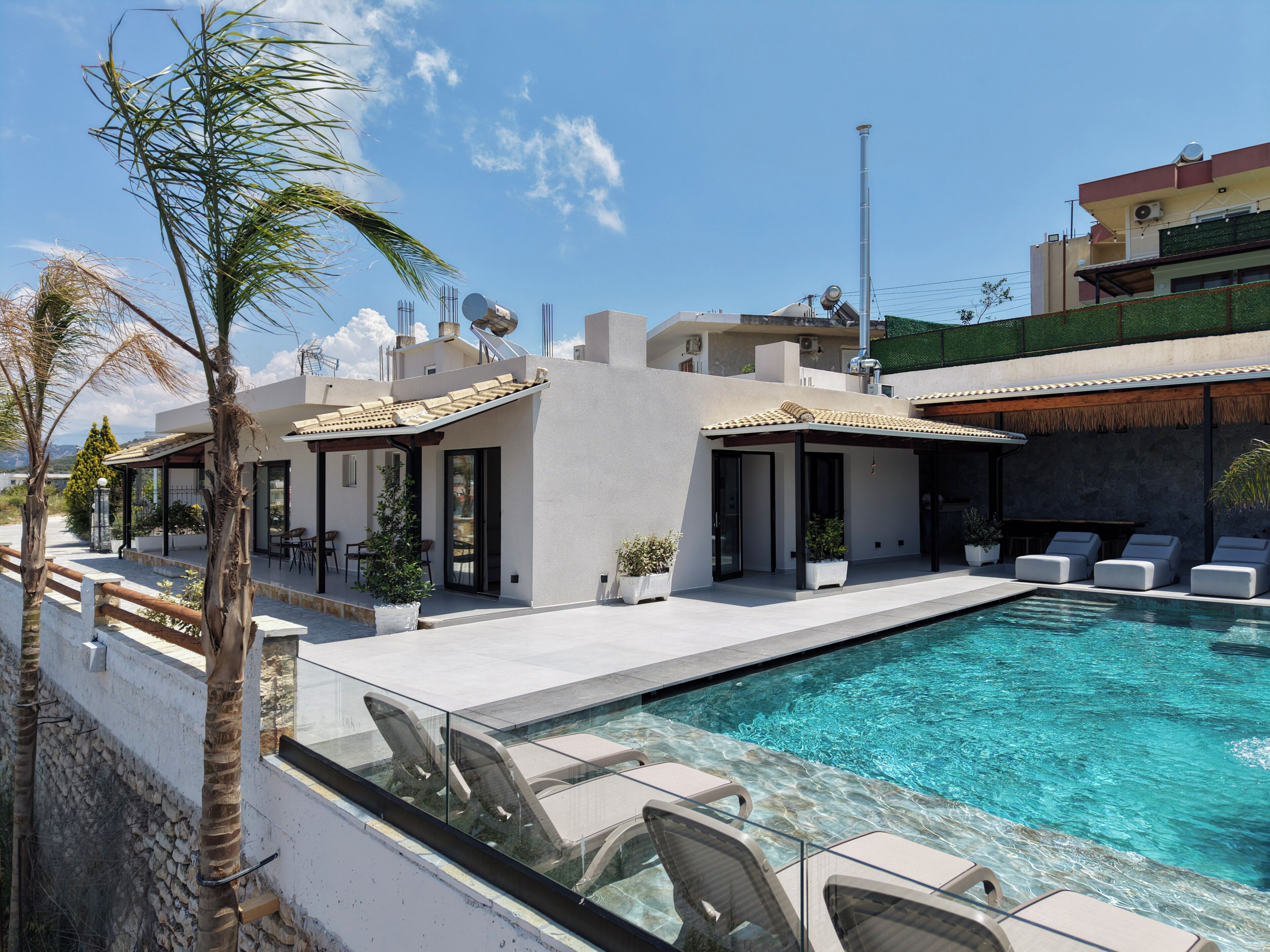 Un área moderna junto a la piscina con sillones de descanso, una alberca y un edificio con techo plano y ventanas amplias.