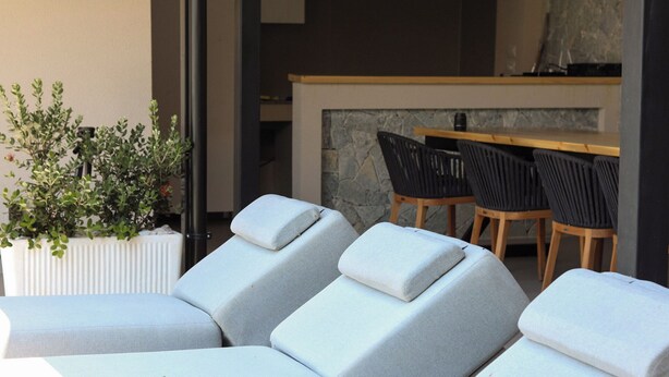 A modern outdoor seating area with cushioned lounge chairs and a stone wall backdrop. - Luxury Villa Oasis (Ksamil)