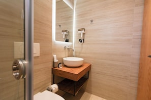Een moderne badkamer met een ronde wastafel, een spiegel, een zeepdispenser en een toilet.