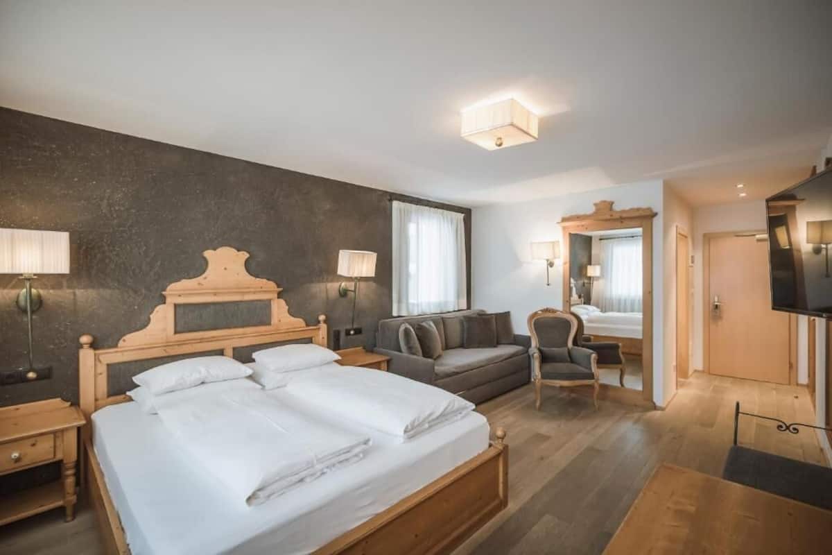 A hotel room with a large bed, a sofa, a desk, and a television.