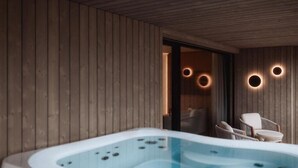 Un espace spa moderne doté d’un jacuzzi, de murs recouverts de panneaux en bois et de deux fauteuils confortables.