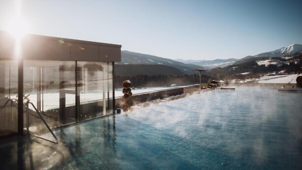 Une piscine d’eau chaude entourée de parois de verre, offrant une vue sur des montagnes enneigées.