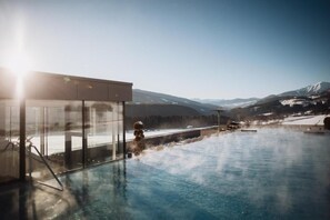 A hot spring pool with a glass enclosure and a view of snow-capped mountains.