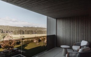 A balcony with a view of a forested landscape, a small table, and two chairs.