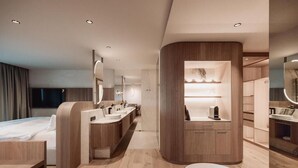 Une chambre d’hôtel moderne dotée d’une coiffeuse aux lignes courbes, d’un grand lit et d’un coin salon séparé.
