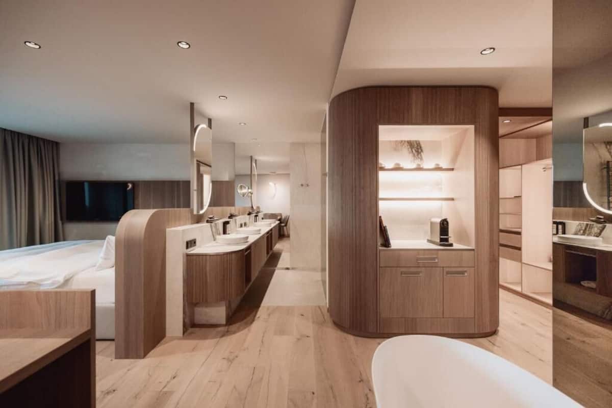 A modern hotel room with a curved vanity, a large bed, and a separate sitting area.