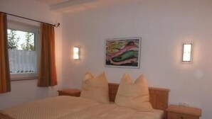 Ein Schlafzimmer mit Bett, Nachttischen, einem Fenster mit Vorhängen und einem Wandbild.