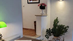 Ein Flur mit Schreibtisch, Lampe, einem gerahmten Bild, einer Vase mit Blumen und einem Topfpflanzen.