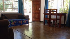 A room with a wooden floor, a sofa with a blue cover, a wooden chair, and a table with a blue curtain. - blue Waxbill Lodge  (South Luangwa National Park)