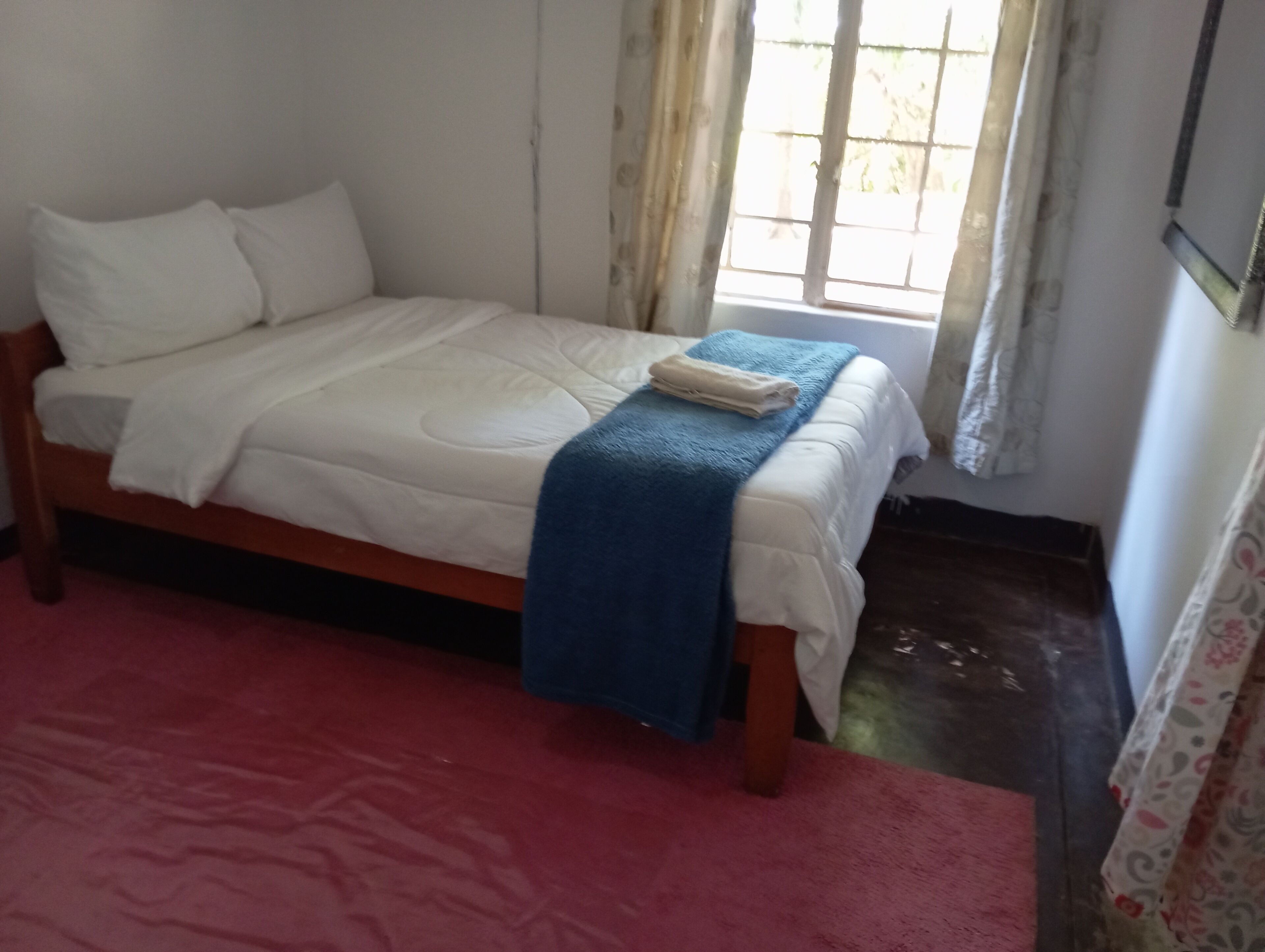 Una cama individual con una manta azul, almohadas blancas y una toalla blanca doblada.