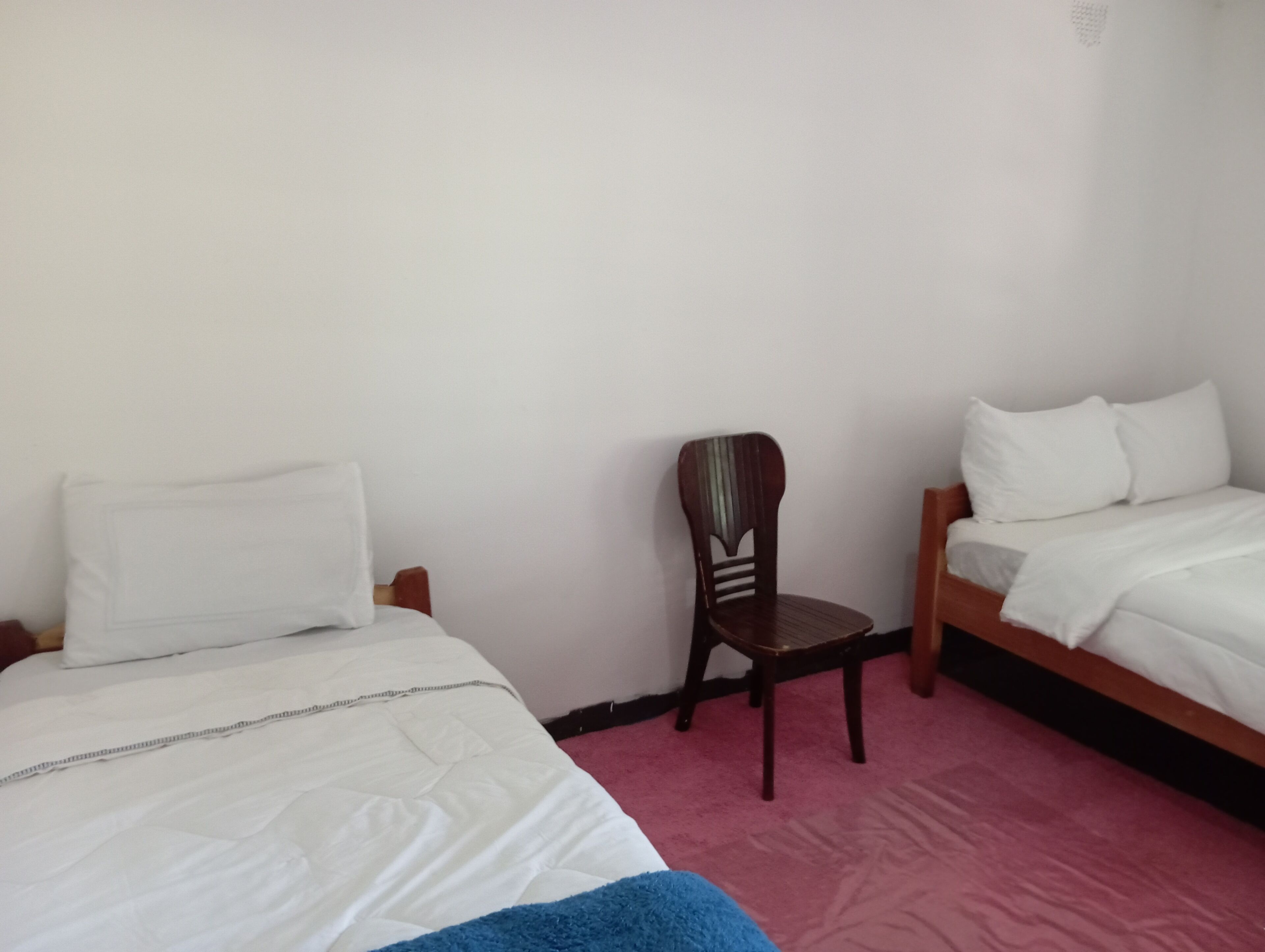 Une chambre avec deux lits, une chaise en bois et un tapis rouge.