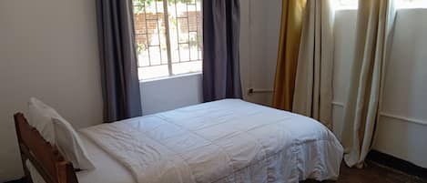 A single bed with a wooden frame, a white bedspread, and a brown patterned rug on the floor.