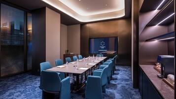 Una sala de conferencias con una mesa larga, sillas azules, una pantalla mostrando 'CRYSTAL ORANGE' y una máquina de café.