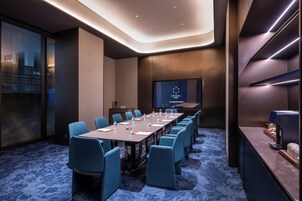 A conference room with a long table, blue chairs, a screen displaying 'CRYSTAL ORANGE,' and a coffee machine.