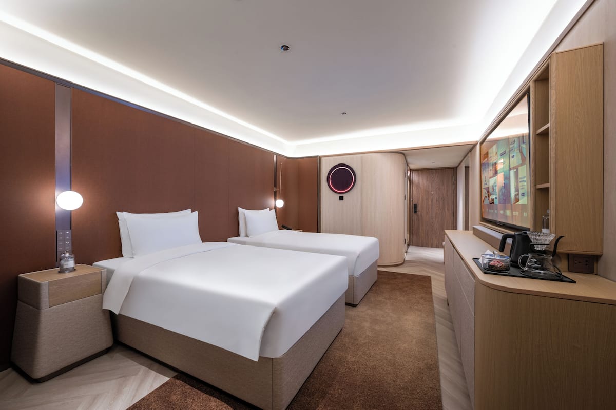 A hotel room with two beds, a desk, a mirror, and a television.