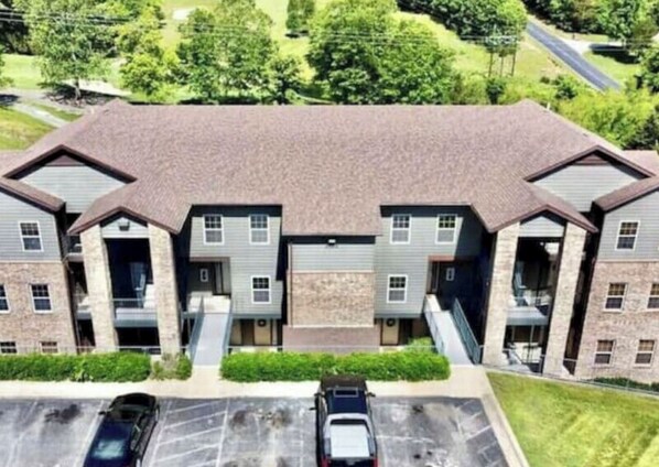 A multi-story residential building with a central garage, multiple entry points, and a parking area with two cars. - FW15, Prime Golf View 1BR - No Stairs! Walk to Pool & Amenities (Branson West)