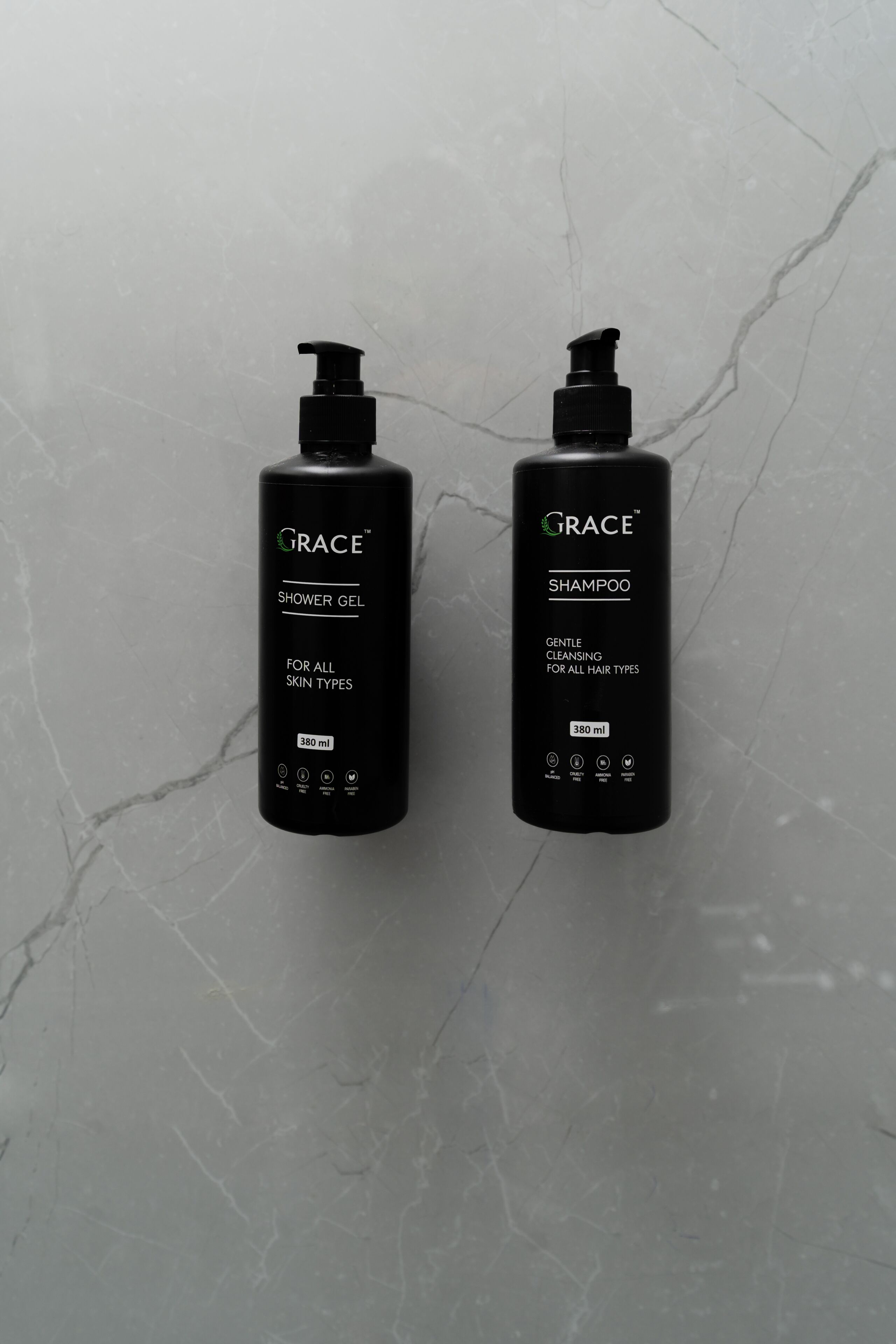 Zwei schwarze Flaschen mit GRACE Duschgel und Shampoo auf einer Marmorplatte.