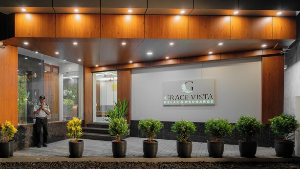 Entrada de hotel con un letrero que dice 'GRACE VISTA', plantas en macetas y un guardia de seguridad.