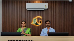 Un mostrador de recepción con un panel de pared de madera, una unidad de aire acondicionado y un logotipo con una hoja y una 'G'.