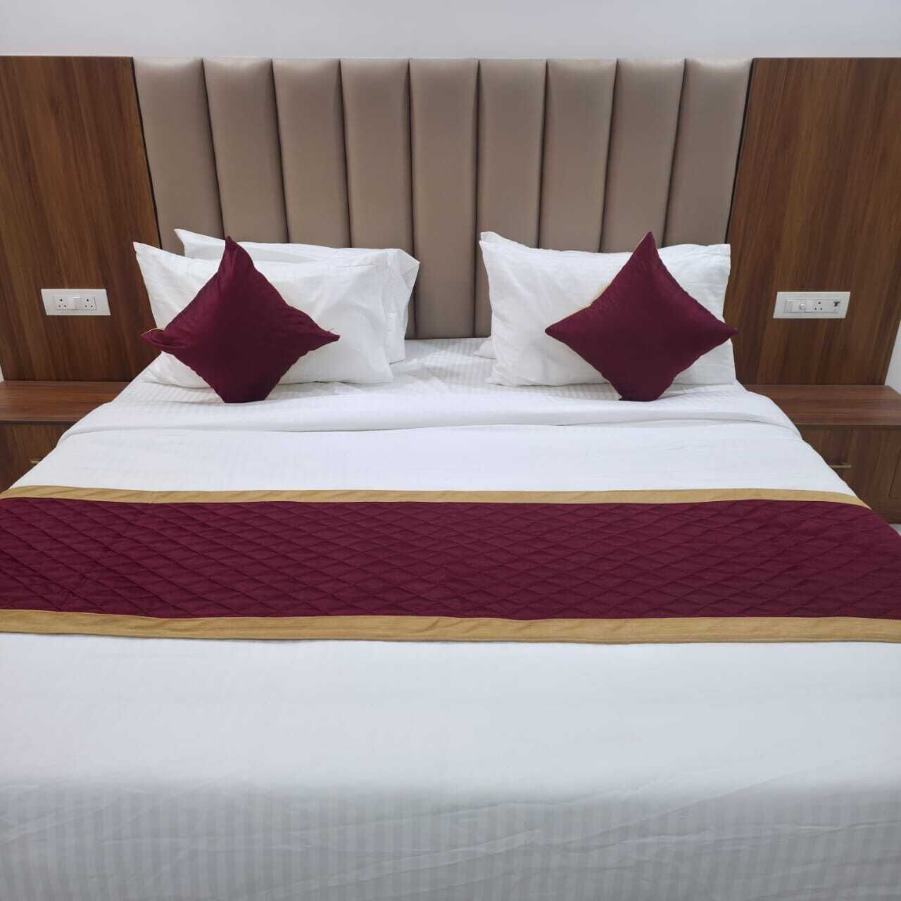 A bed with a headboard, white bedding, two pillows, and a maroon blanket.