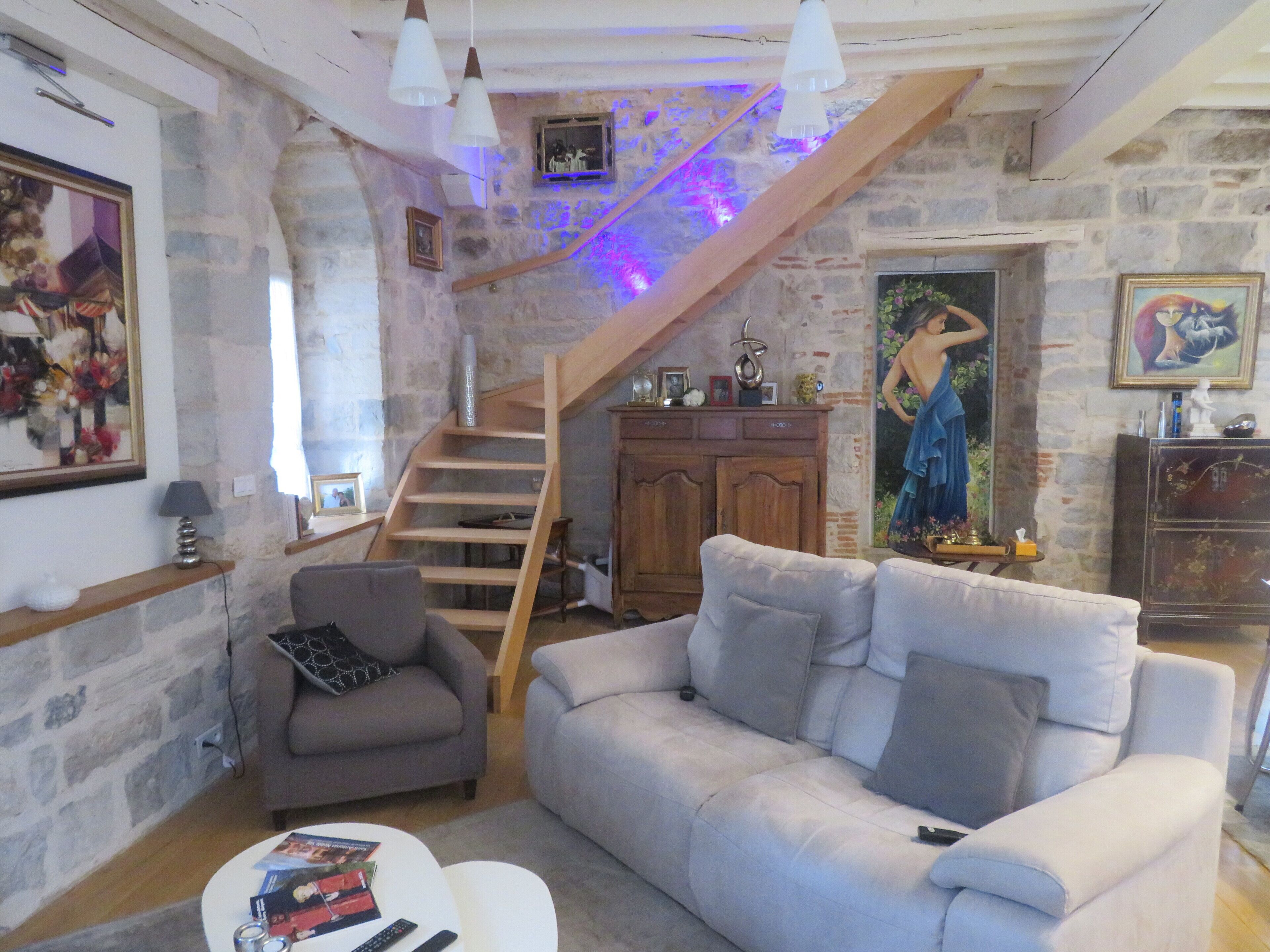Een gezellige woonkamer met een stenen muur, een houten trap, een grijze bank, een kleine fauteuil en een witte salontafel.