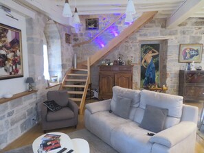 Ein gemütliches Wohnzimmer mit einer Steinwand, einer Holztreppe, einem grauen Sofa, einem kleinen Sessel und einem weißen Couchtisch.