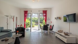 Una sala moderna con sofá, una mesa de centro, televisor, comedor y vistas al verdor a través de las ventanas.