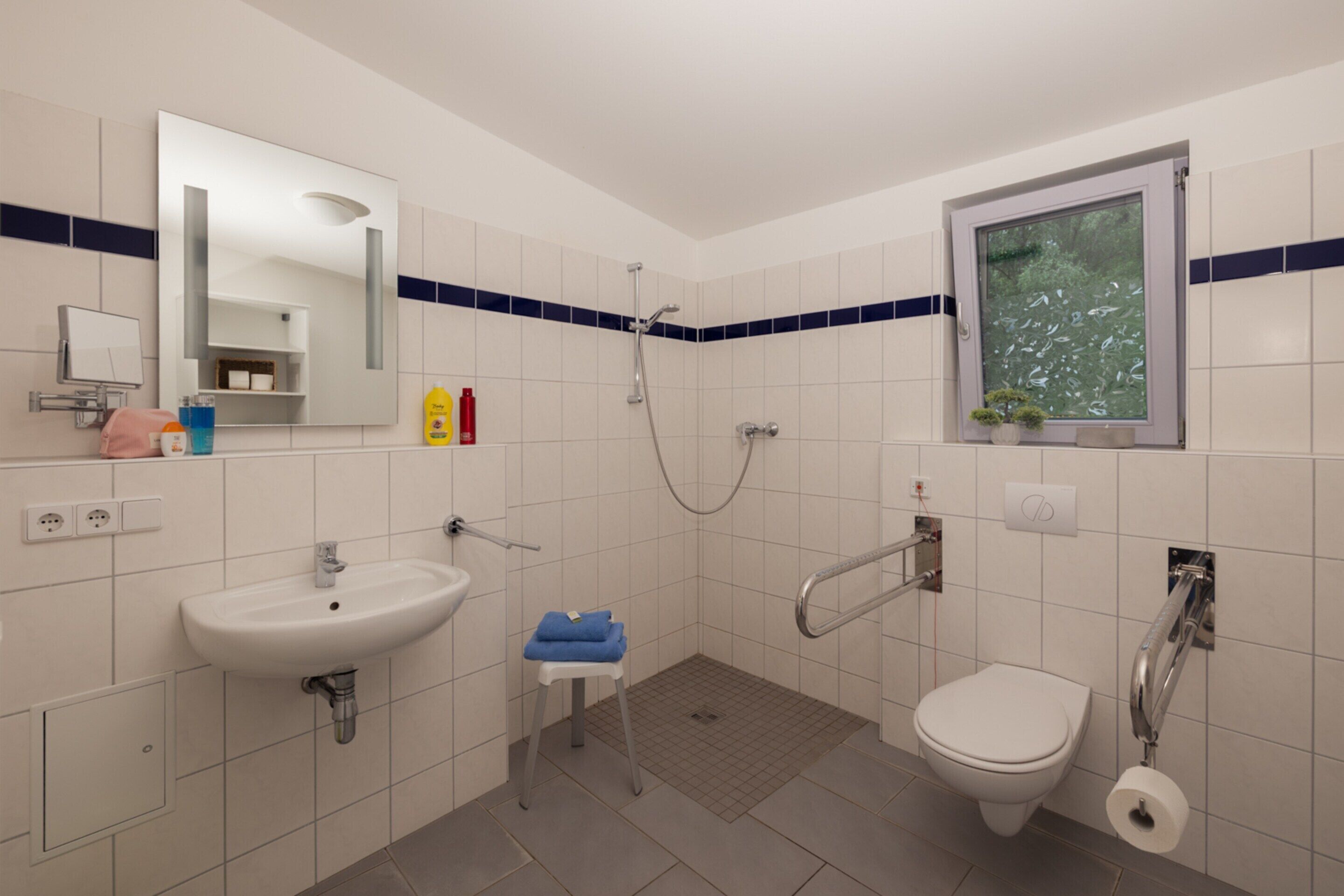 Een badkamer met een wastafel, toilet, douche en een raam met uitzicht op bomen.