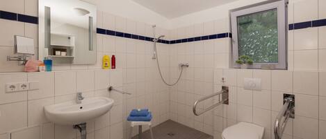 Een badkamer met een wastafel, toilet, douche en een raam met uitzicht op bomen.
