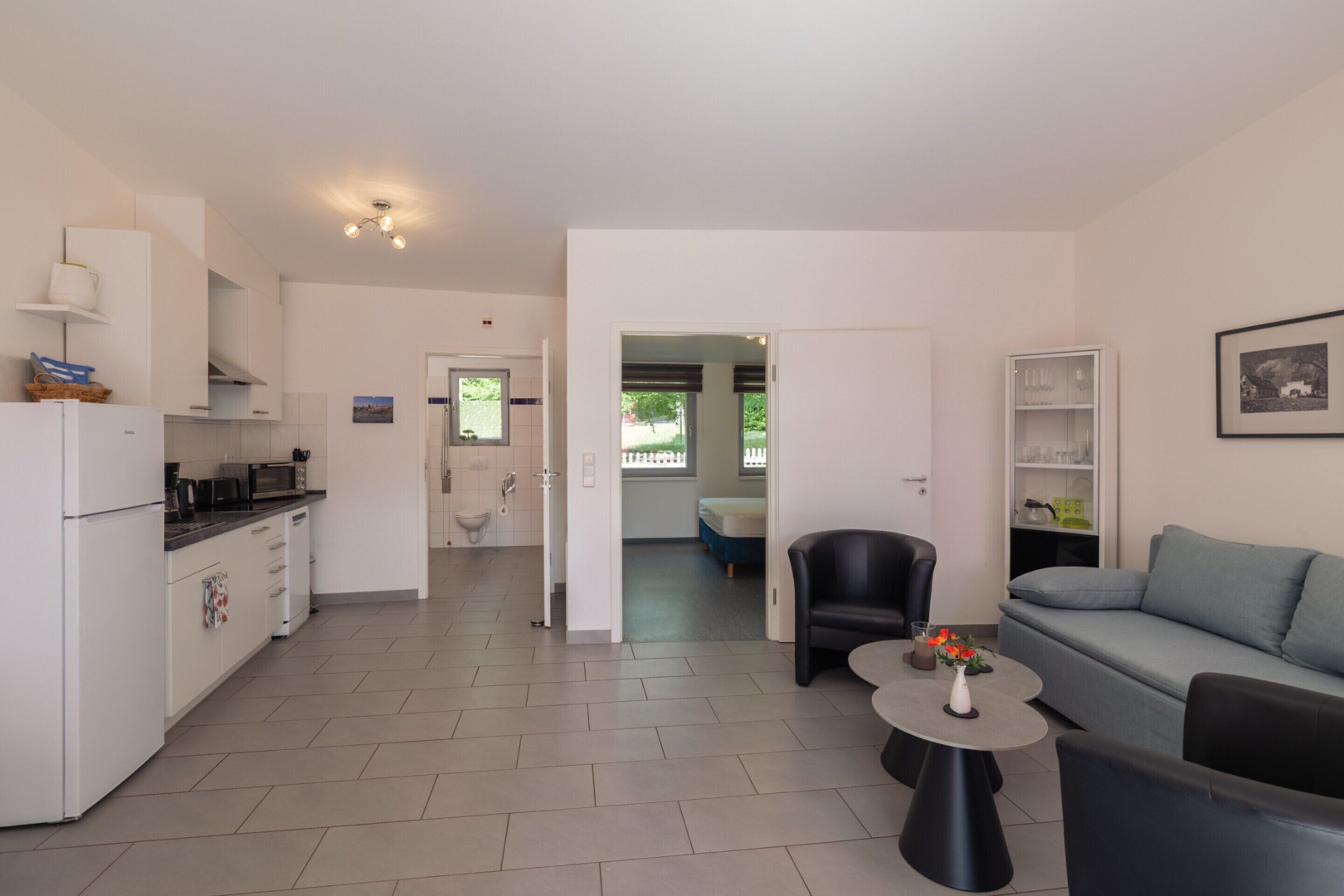 A modern kitchen with white appliances, a dining area with a black chair and a small round table, and a light blue sofa.