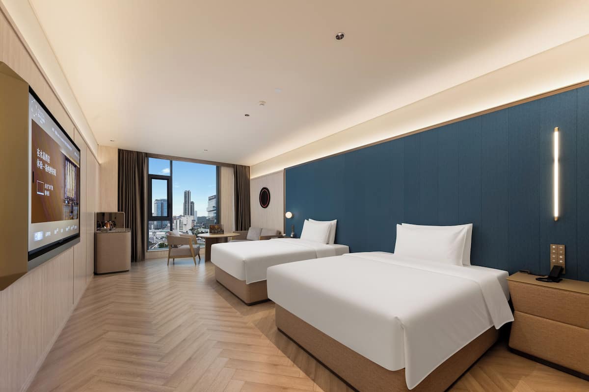 Habitació d'hotel amb dos llits, escriptori, cadira, televisió i vista a la ciutat.