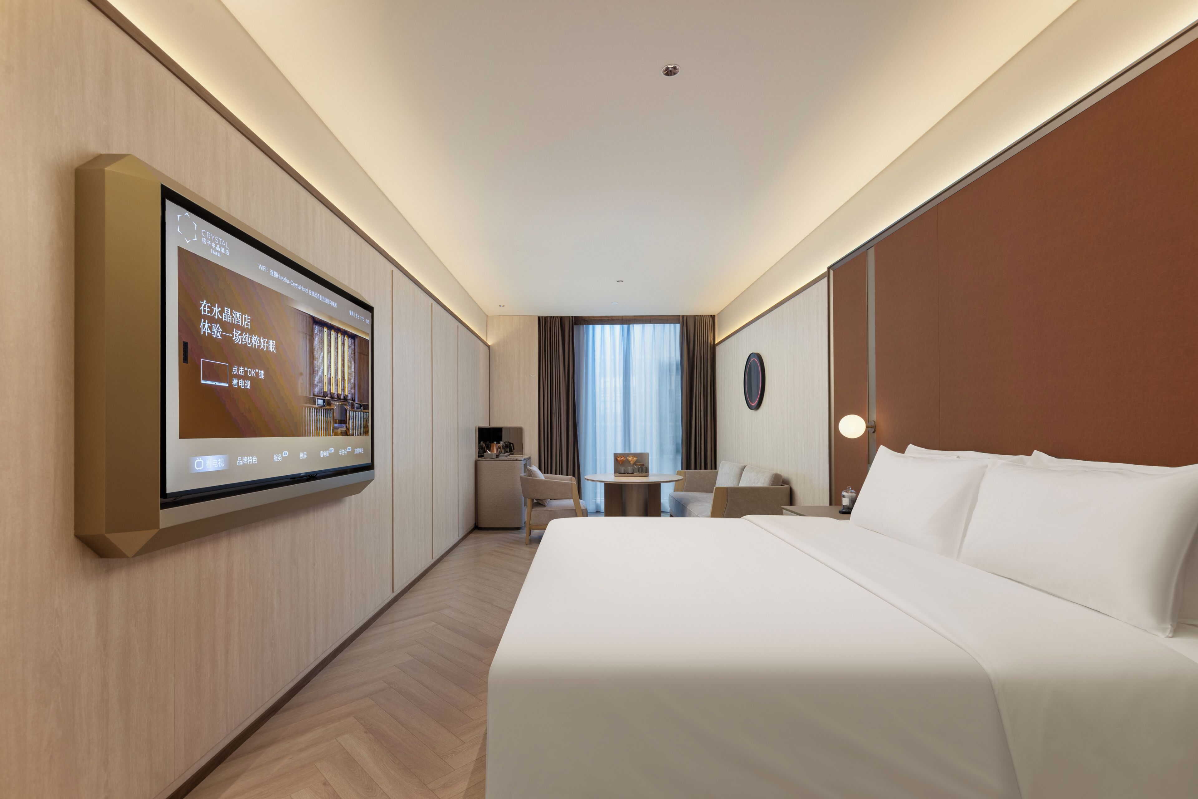Habitación de hotel con una cama grande, un escritorio, una silla, un televisor de pantalla plana montado en la pared y una ventana con cortinas.
