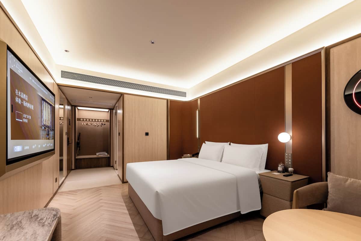 Habitació d'hotel amb un llit gran, una taula de nit, televisió i vista al passadís.