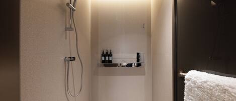 A modern shower with a handheld showerhead, a wall-mounted faucet, and a shelf with toiletries.