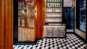 Una zona de bar con suelo de cuadros, barra y estantes con botellas.