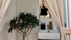 A bathroom with a mirror, a sink, toiletries, and a potted plant. - Peanuts Home Le Lai - Chic Local Stay, Steps to Ben Thanh & Bui Vien (Ho Chi Minh city)