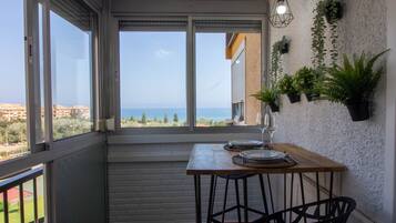 A balcony with a view of the sea, a table with plates and a glass, and potted plants on the wall.