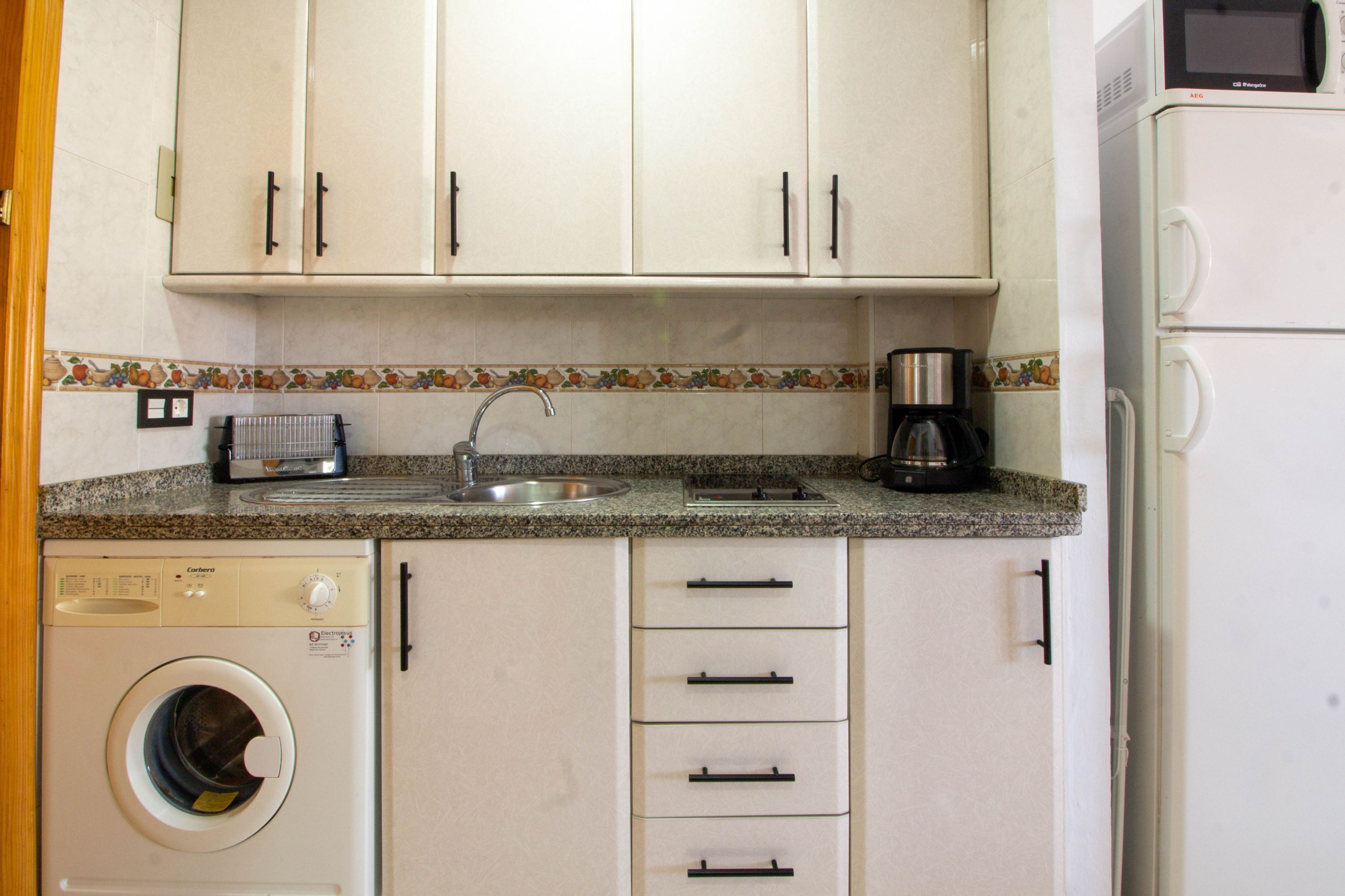 Une cuisine compacte équipée d’un lave-linge, d’une machine à café et d’un four à micro-ondes.