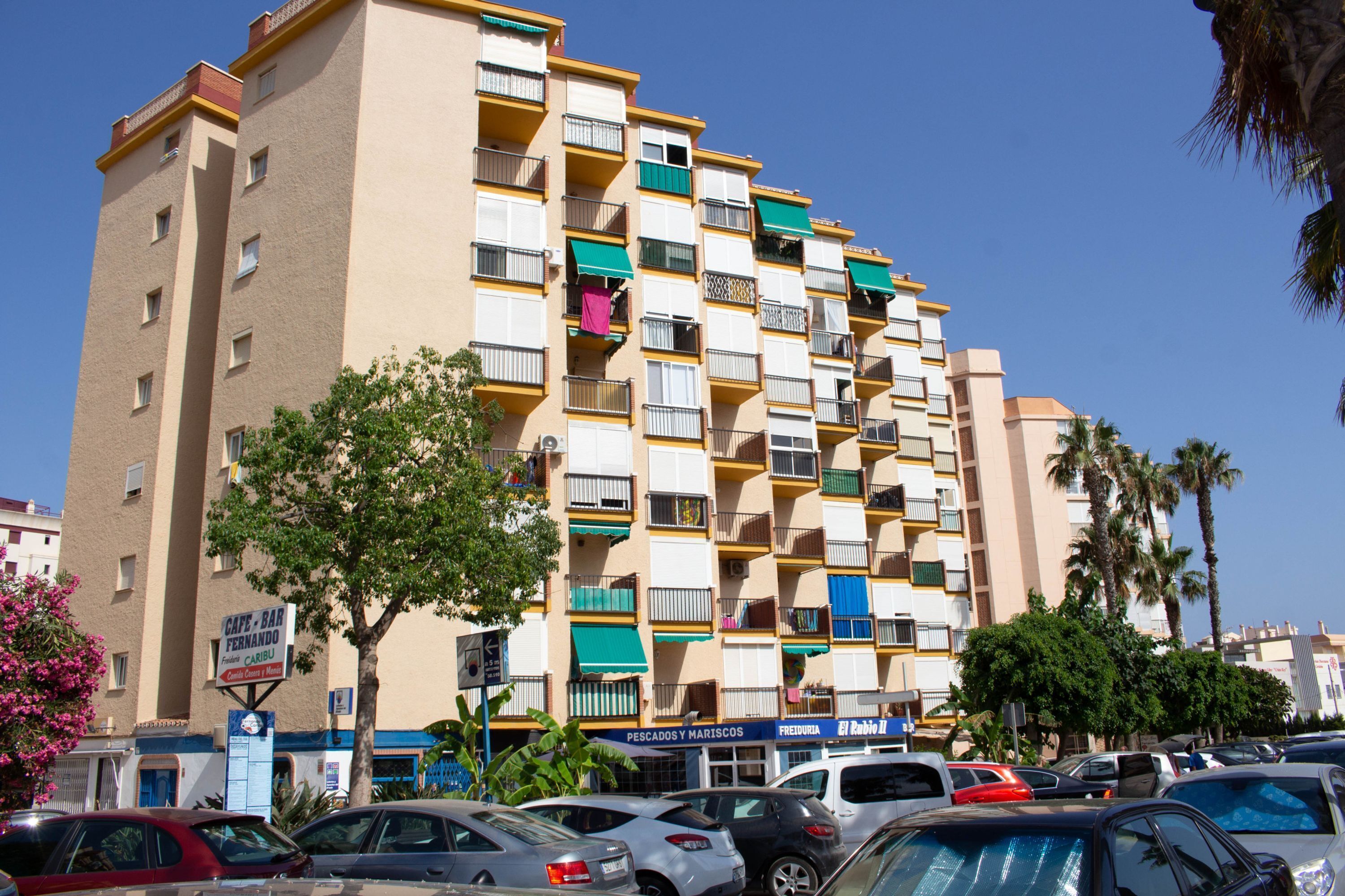 A multi-story building with balconies, a sign for 'Café-Bar Fernando,' and several parked cars.