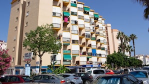 Un edificio de varios pisos con balcones, un cartel que dice 'Café-Bar Fernando' y varios coches aparcados.
