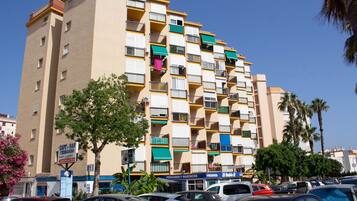 A multi-story building with balconies, a sign for 'Café-Bar Fernando,' and several parked cars.