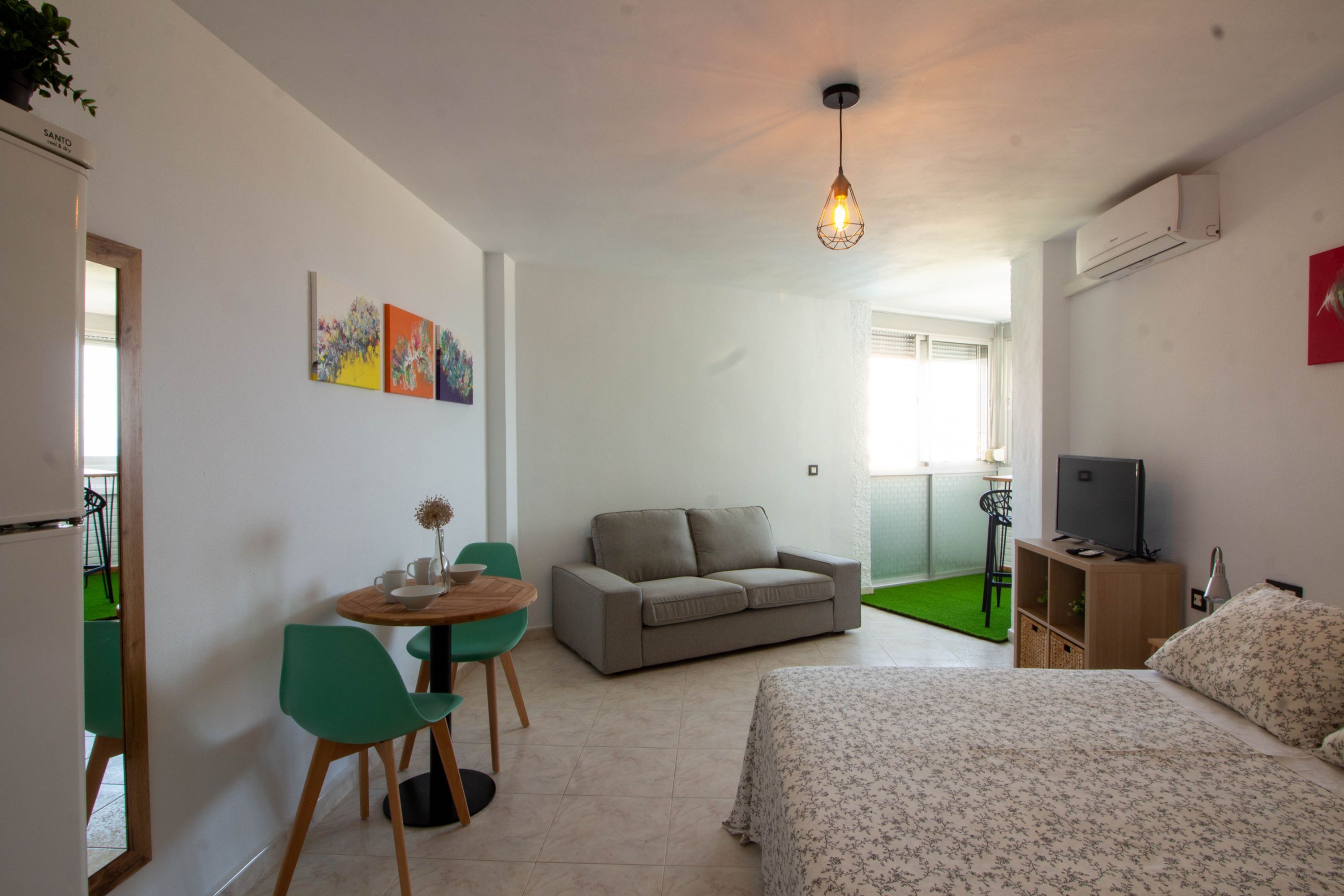 A room with a bed, a sofa, a dining table with chairs, a TV, and artwork on the wall.