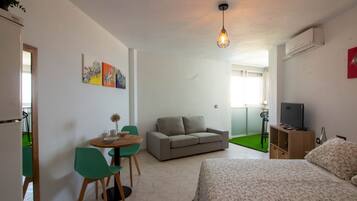 A room with a bed, a sofa, a dining table with chairs, a TV, and artwork on the wall.