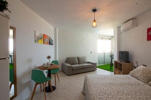 Ein Zimmer mit Bett, Sofa, Esstisch mit Stühlen, Fernseher und Kunstwerken an der Wand.