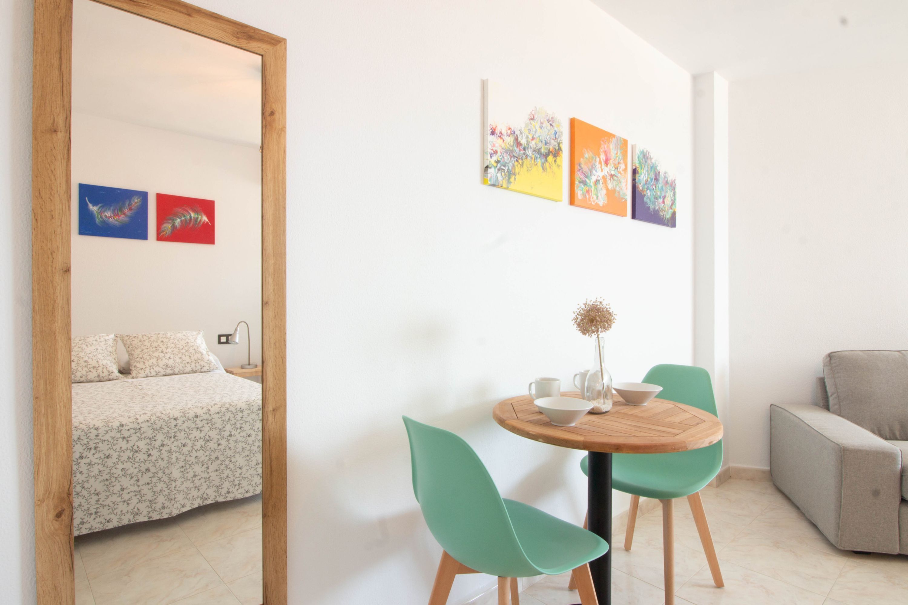 A room with a bed, a round wooden table with chairs, a small sofa, and artwork on the wall.