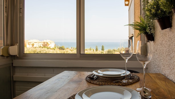 Mesa para dos personas, con platos, cubiertos y copas de vino, con vista al mar.