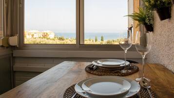 A table set for two with plates, cutlery, and wine glasses, overlooking a coastal view.