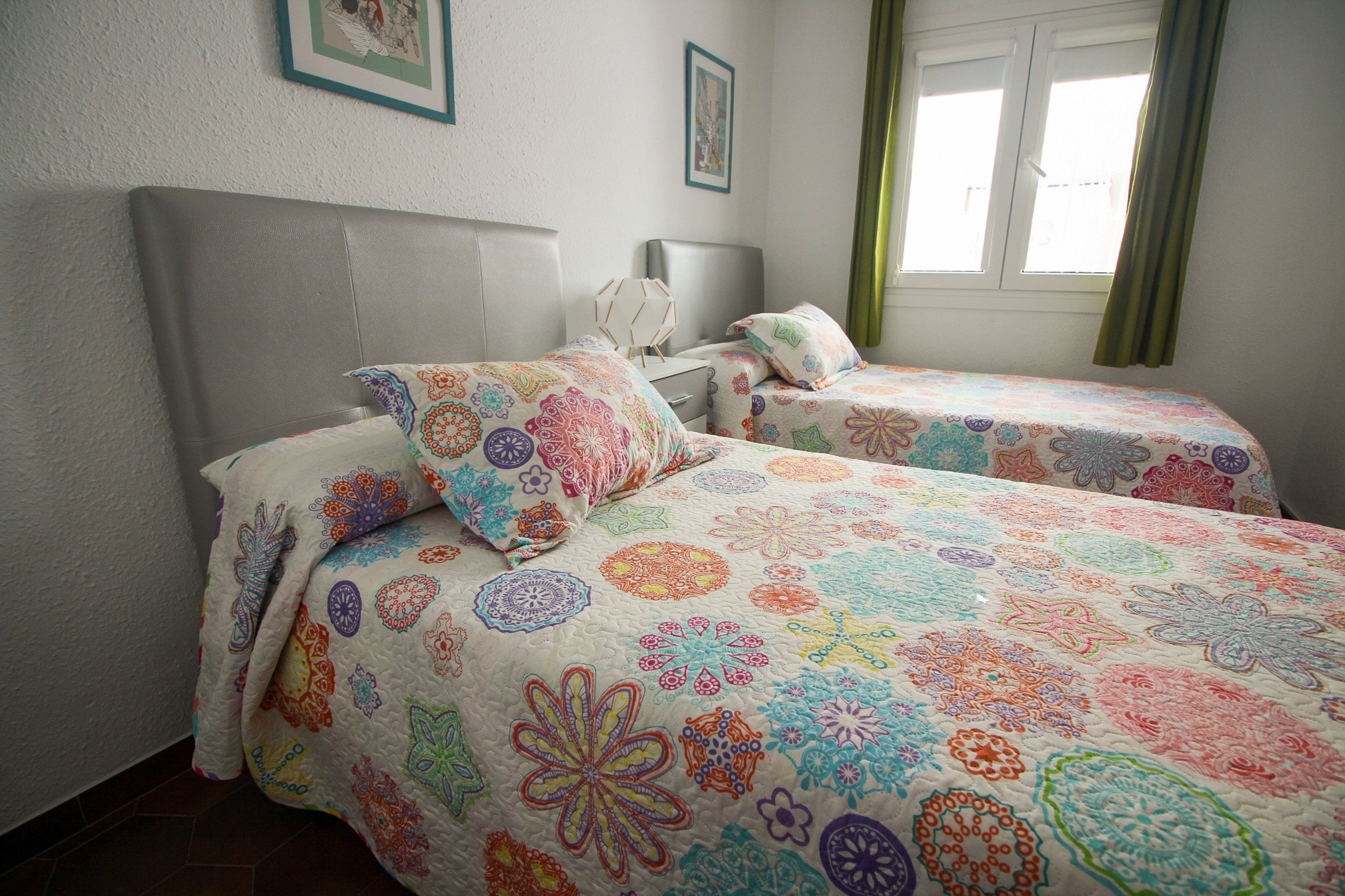 A bedroom with two beds, a window with curtains, and a wall with framed pictures.