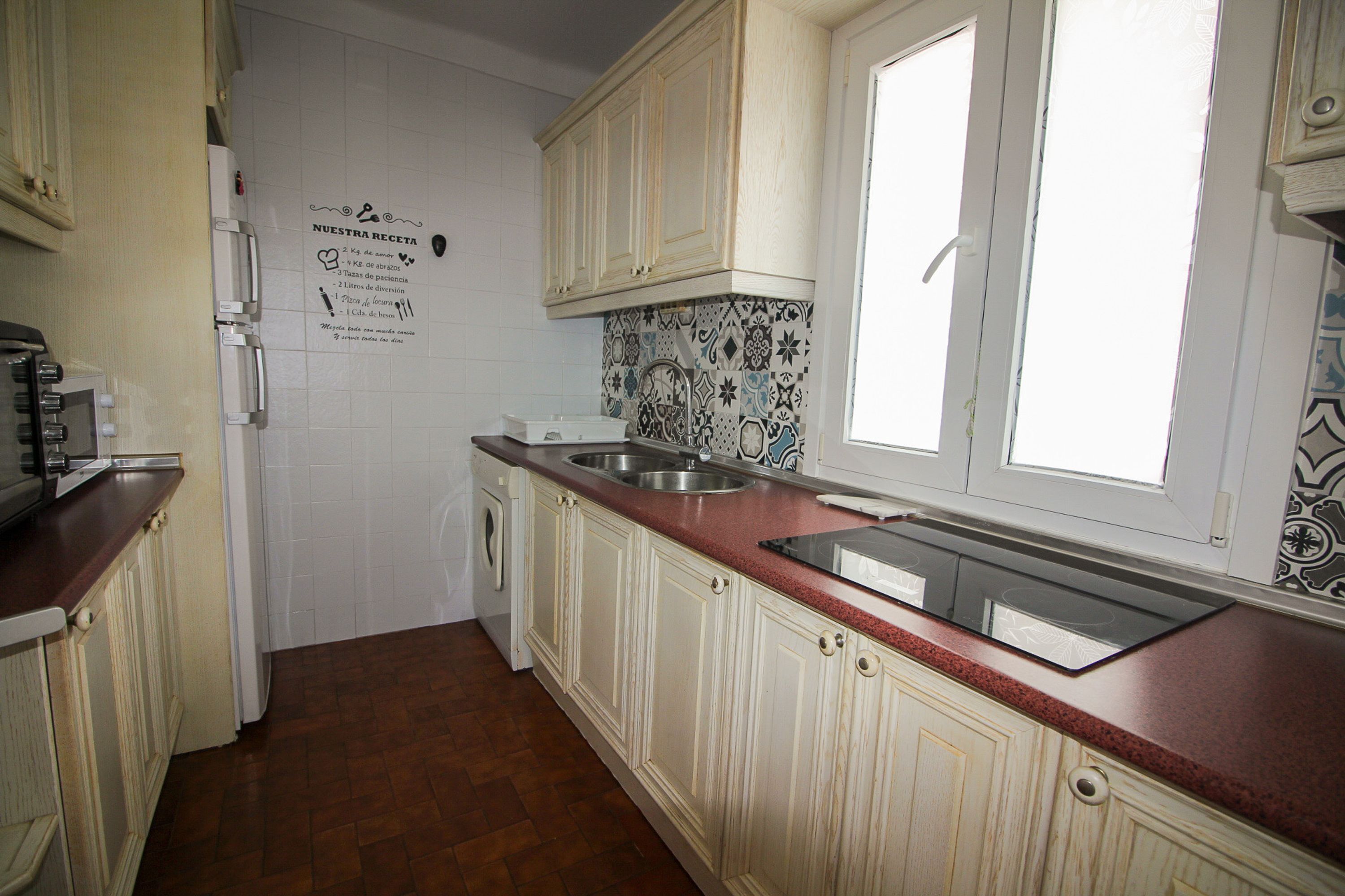 A kitchen with white cabinets, a stainless steel sink, a built-in oven, and a window.